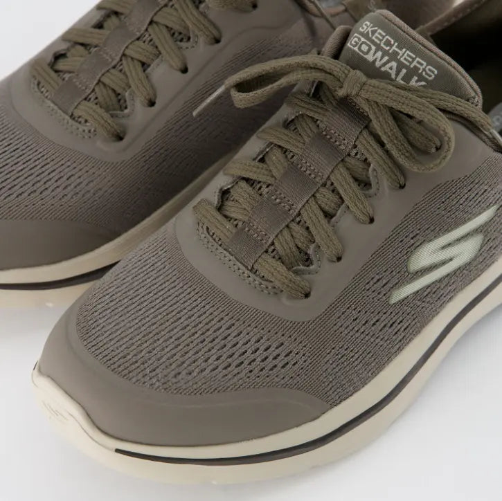 Primer plano de la malla texturizada gris pardo, los cordones elásticos y las etiquetas de lengüeta "Skechers GO WALK", destacando los materiales transpirables.