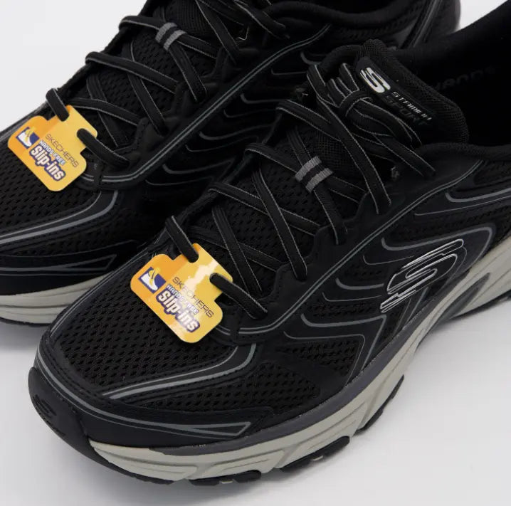 Primer plano de la malla transpirable y cordones elásticos decorativos de las Skechers Stamina Sport negras.