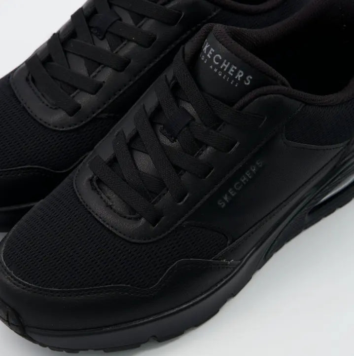 Primer plano de la parte delantera de las zapatillas Skechers Uno Slip-ins negras, mostrando la textura de la malla, el "durabuck" y los cordones elásticos.