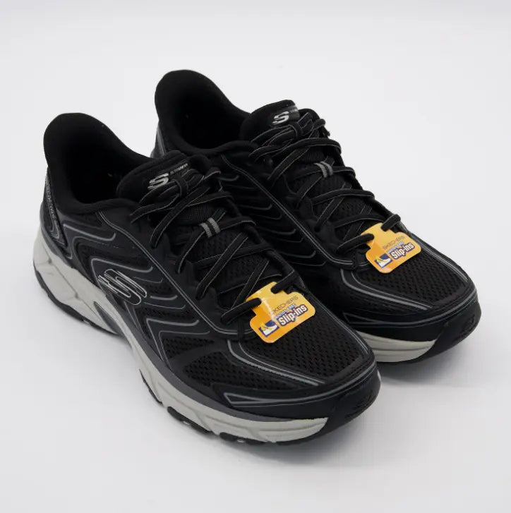 Zapatillas Skechers Hands Free Slip-ins Stamina Sport en color negro con detalles grises y etiquetas amarillas de tecnología manos libres.