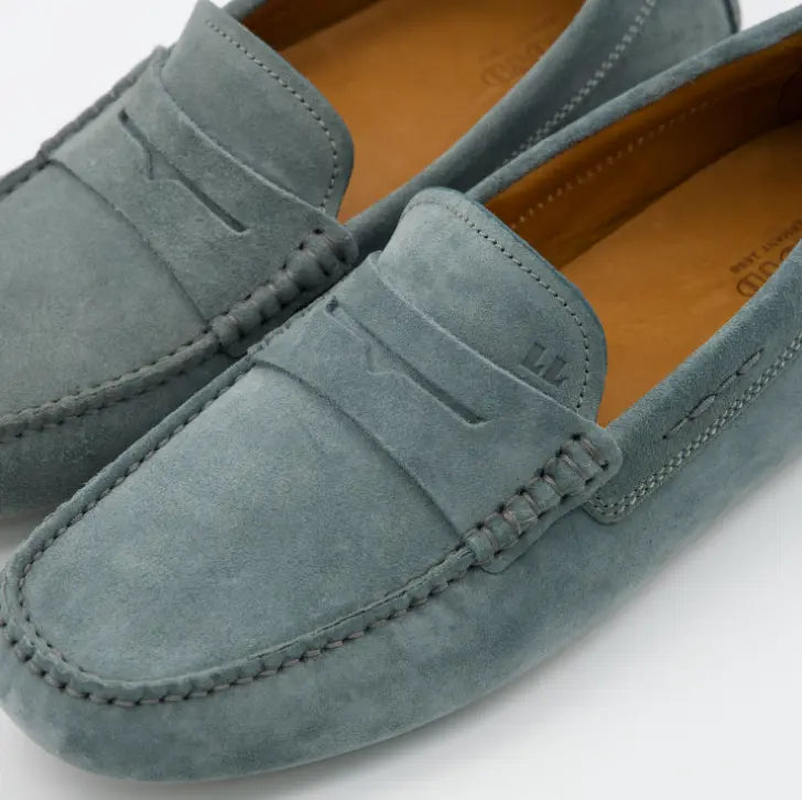 Primer plano de costuras artesanales y detalle LL grabado en mocasín de ante Lloyd azul.